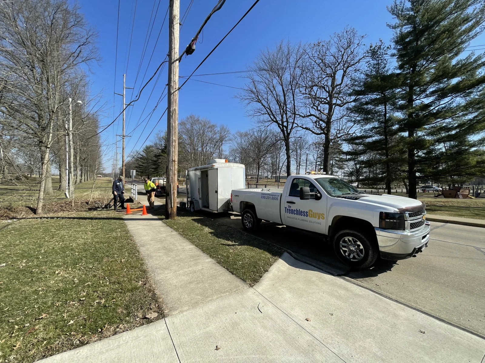 Service truck and technicians installing trenchless drainage equipment at residential property