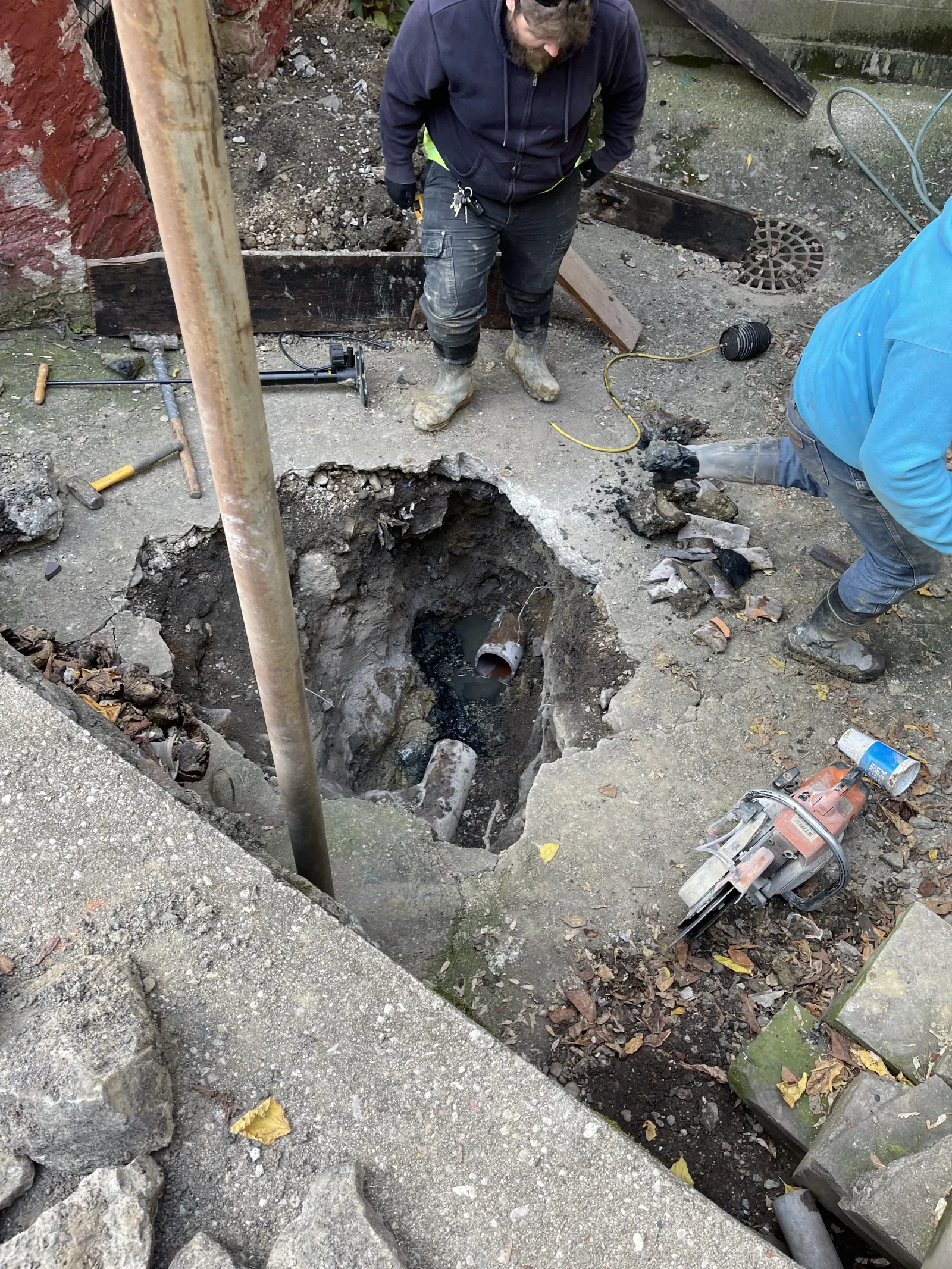 Sewer pipe excavation showing deteriorated underground drainage line with removal debris and replacement work in progress