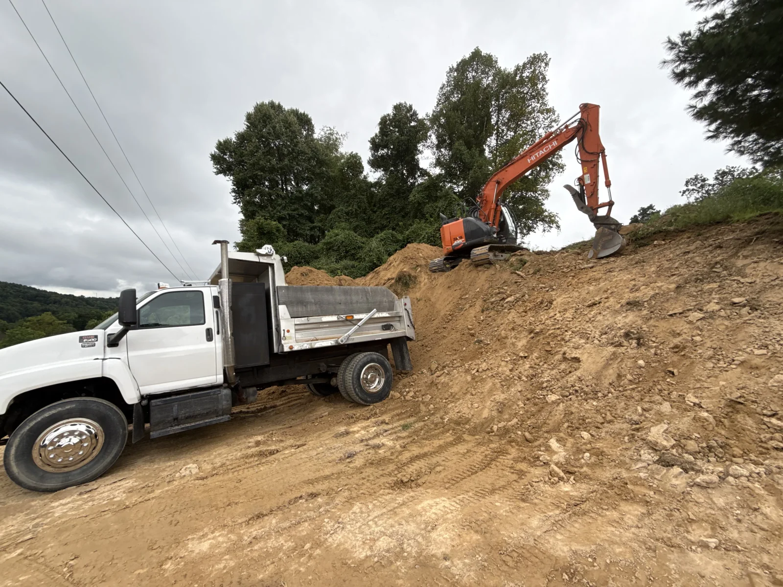 Orange excavator loading soil into white dump truck at construction site