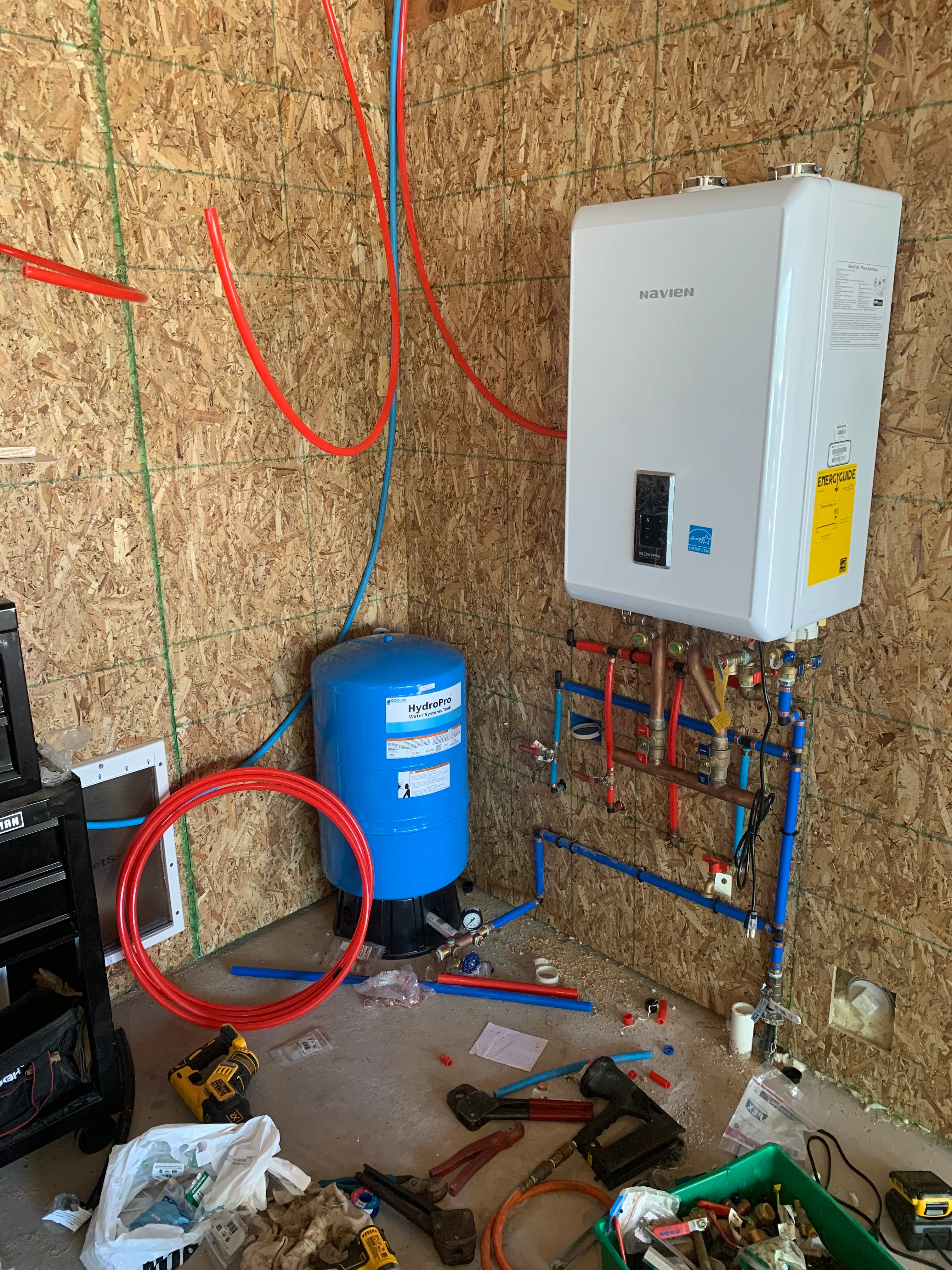 Navien tankless water heater with blue pressure tank and red/blue PEX lines installed on wall