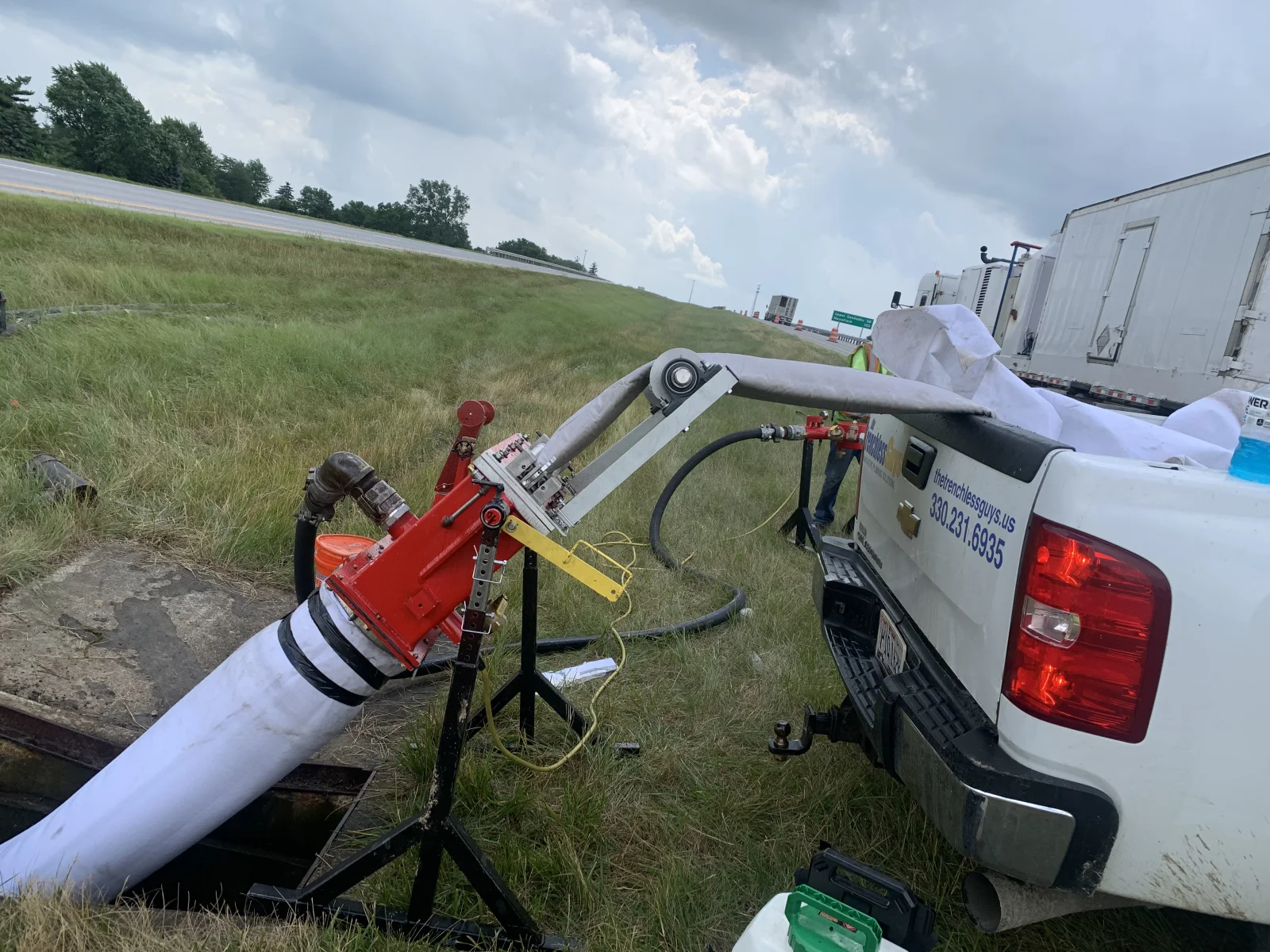 Red pump unit connected to white PVC pipe with hoses for trenchless drainage excavation