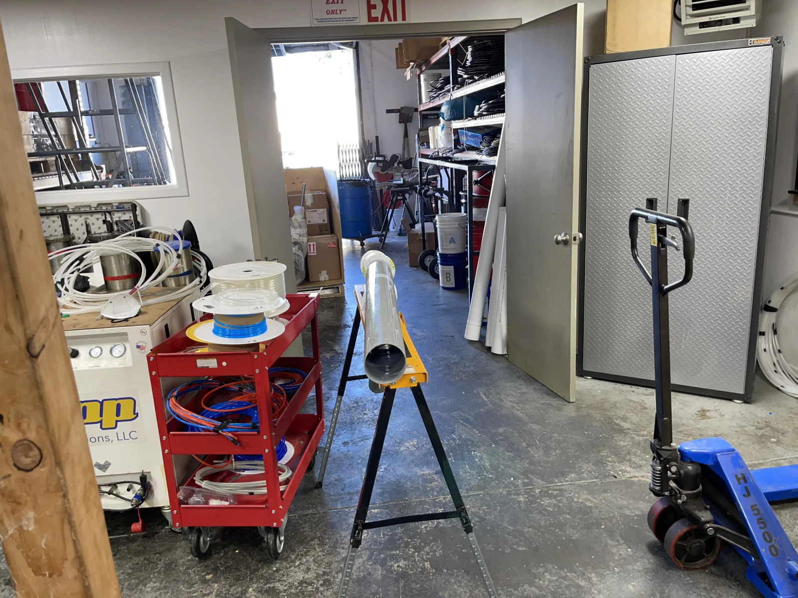 Service equipment including red cart with hoses, inspection camera on tripod, metal storage cabinets, and hydraulic tools in workspace