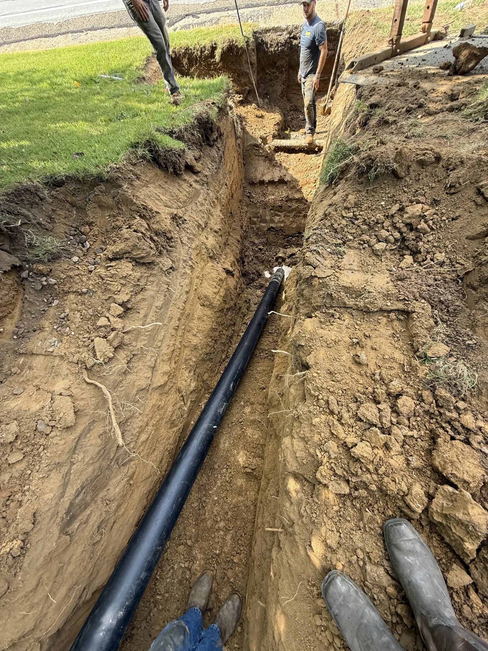 Black drainage pipe installed in deep residential trench with clay soil walls