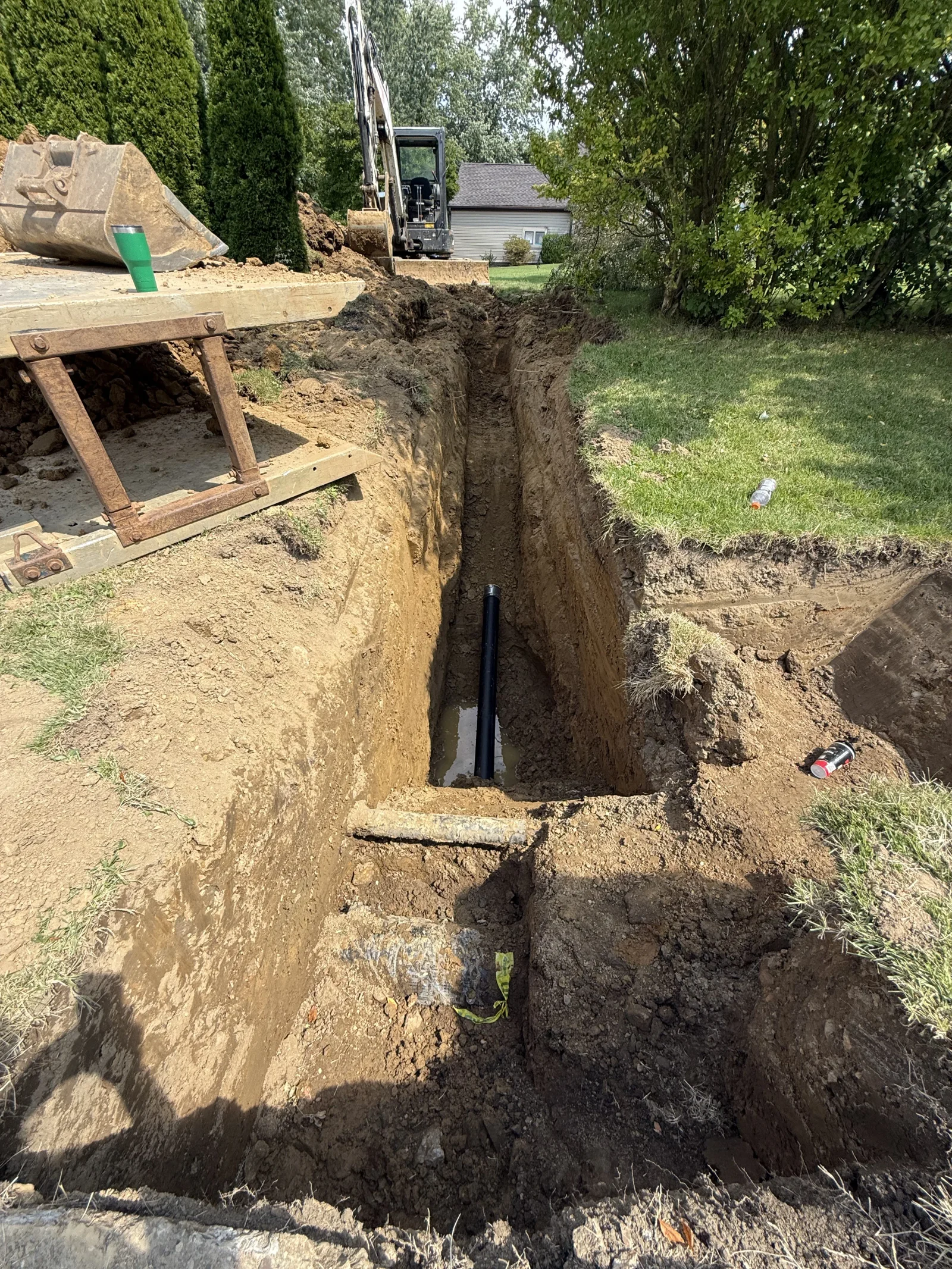Deep residential drainage trench with black pipe installation and excavated soil