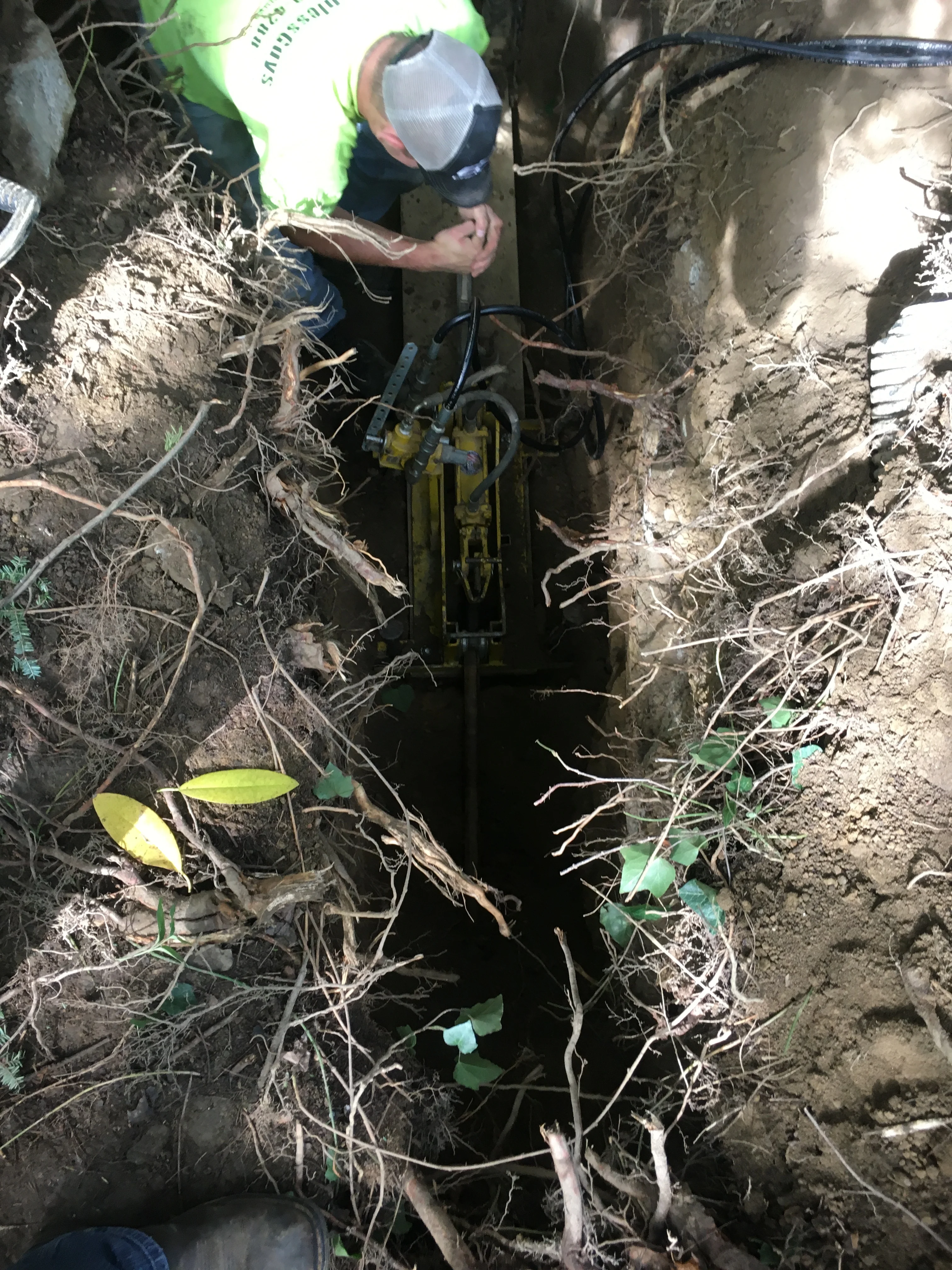 Technician installing yellow underground utility conduit with blue wiring in excavated trench