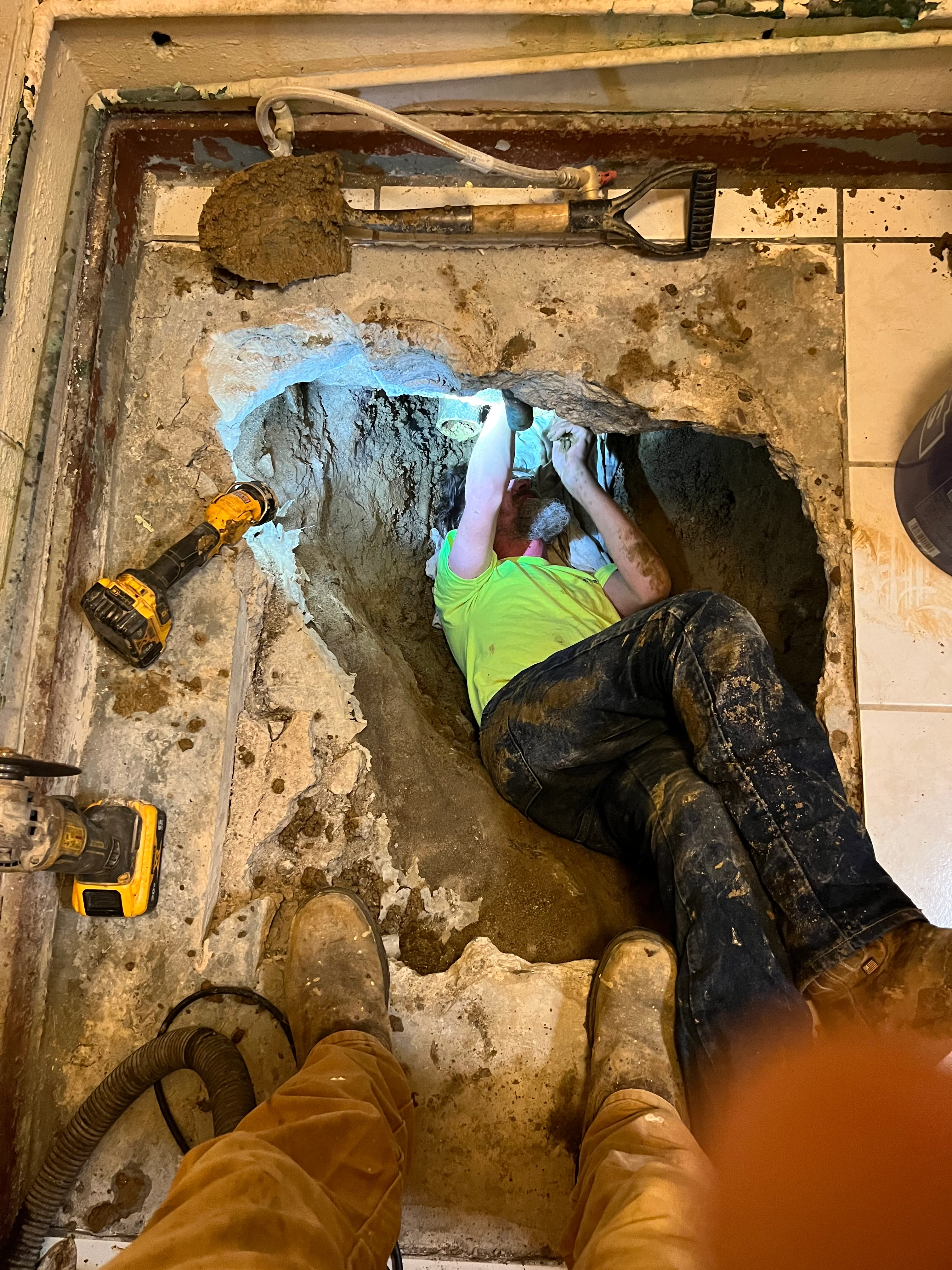 Plumber working in excavated pit installing underground pipes with blue marking paint visible