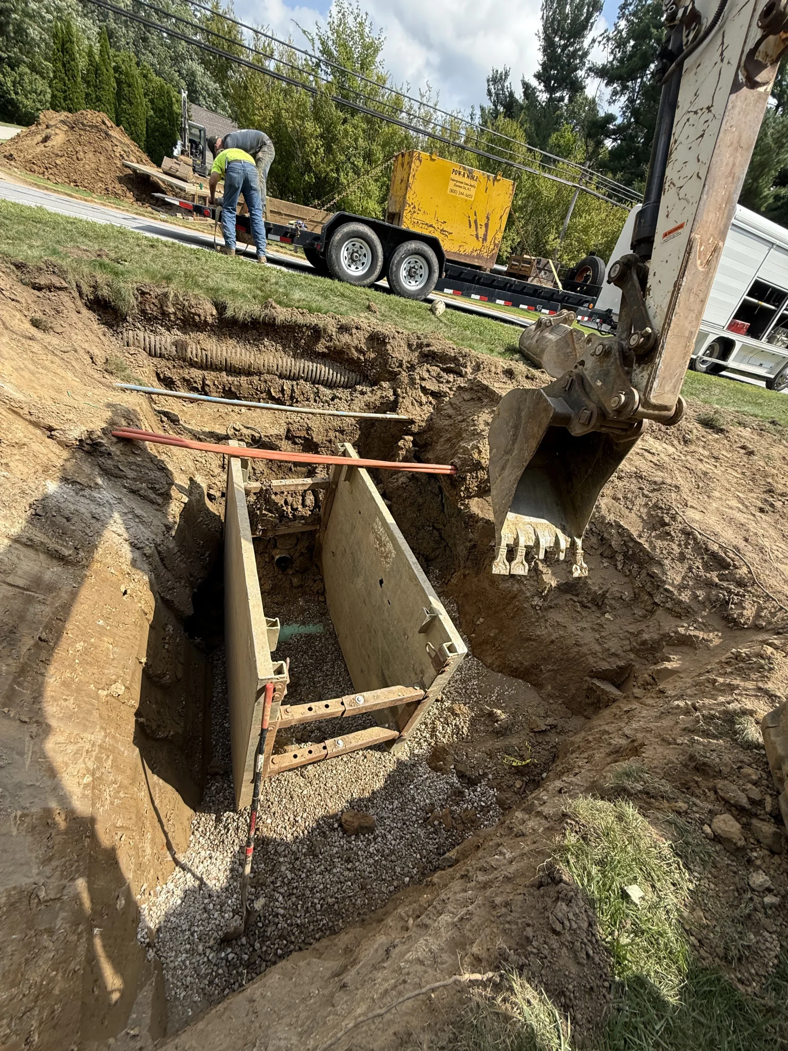 Excavated trench with installed concrete drainage box, gravel base, and heavy equipment on-site