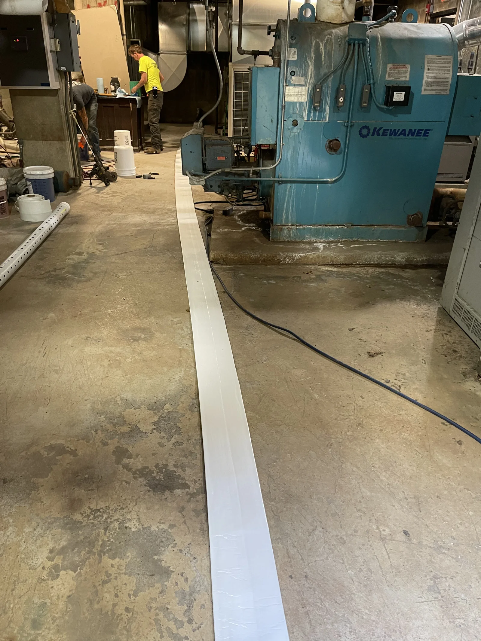 White PVC drainage channel installed on concrete floor in industrial facility with equipment
