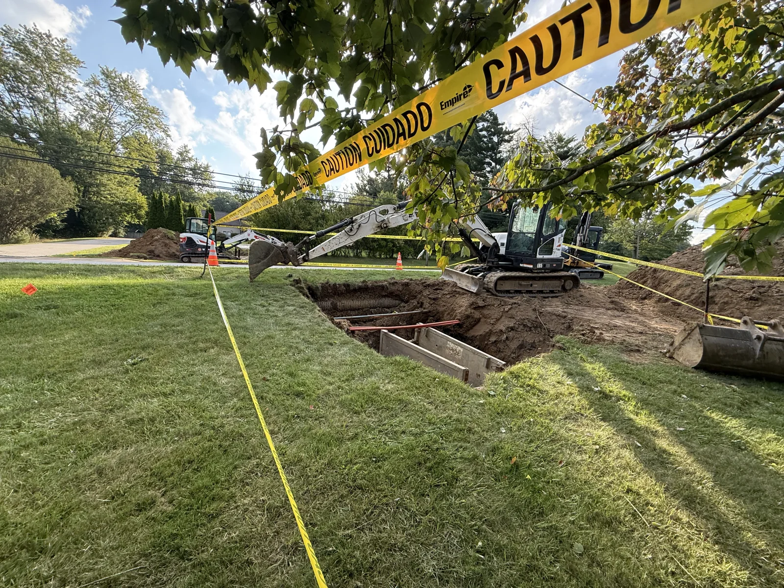 Tracked excavator with steel trench shoring during residential drainage system installation