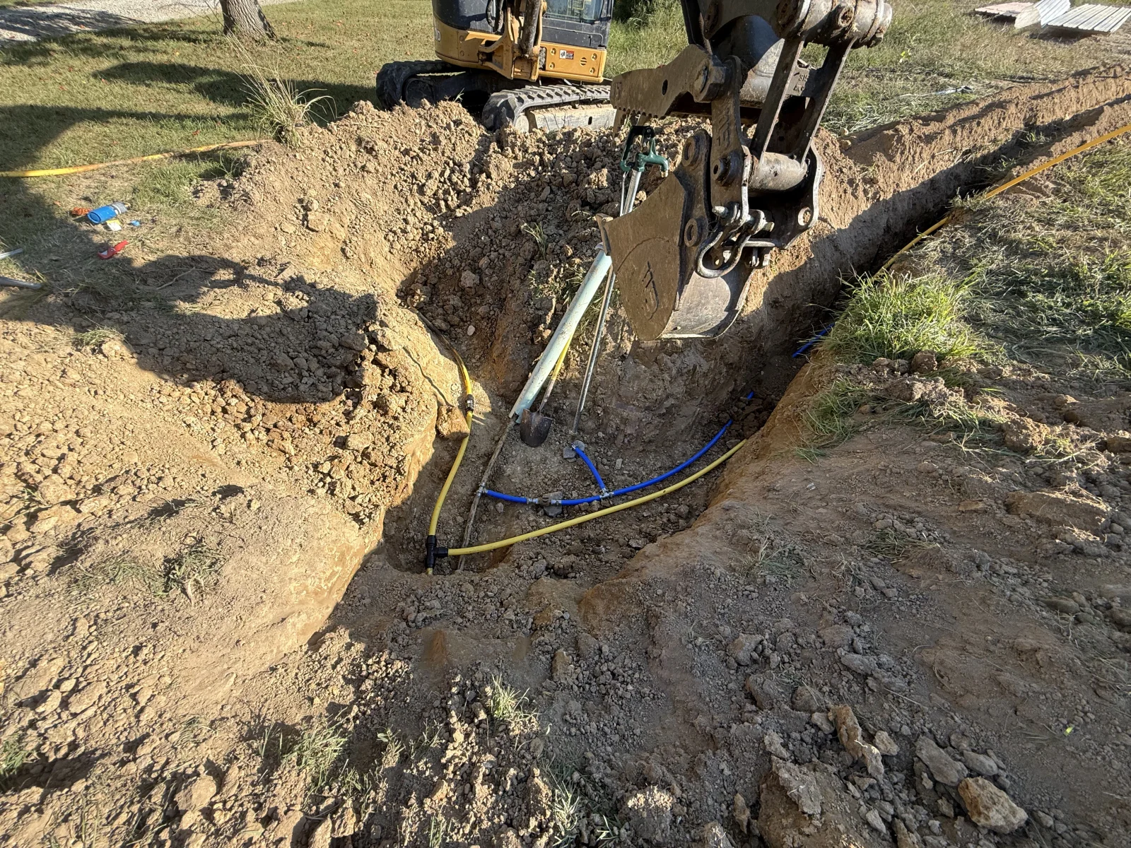 Mini excavator installing yellow and blue utility lines in open trench with proper grading