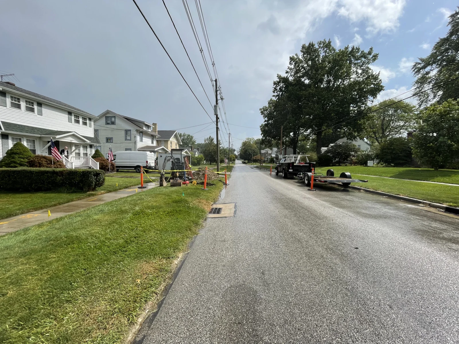 Trench excavation and drainage pipe installation on residential street with utility equipment